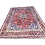 A large Indian rug woven with pink floral field having blue spandrels, framed by brown frieze of