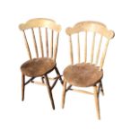 A pair of C20th elm kitchen chairs with shaped arched backs on spindles above circular solid