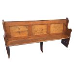 A Victorian pine pew with hymn book shelf on a panelled pack, having shaped ends and plank seat. (