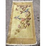 A Chinese silk style rug woven with field of birds and blossom foliage on fawn ground, within a gold