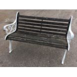 A cast iron garden bench with slatted back and seat framed by scrolled arms, raised on channelled