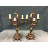 A pair of brass candelabra each with four scrolled branches on decorative urn columns with