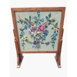 An oak coffee table with floral woolwork tapestry under glass, having folding legs with slide for