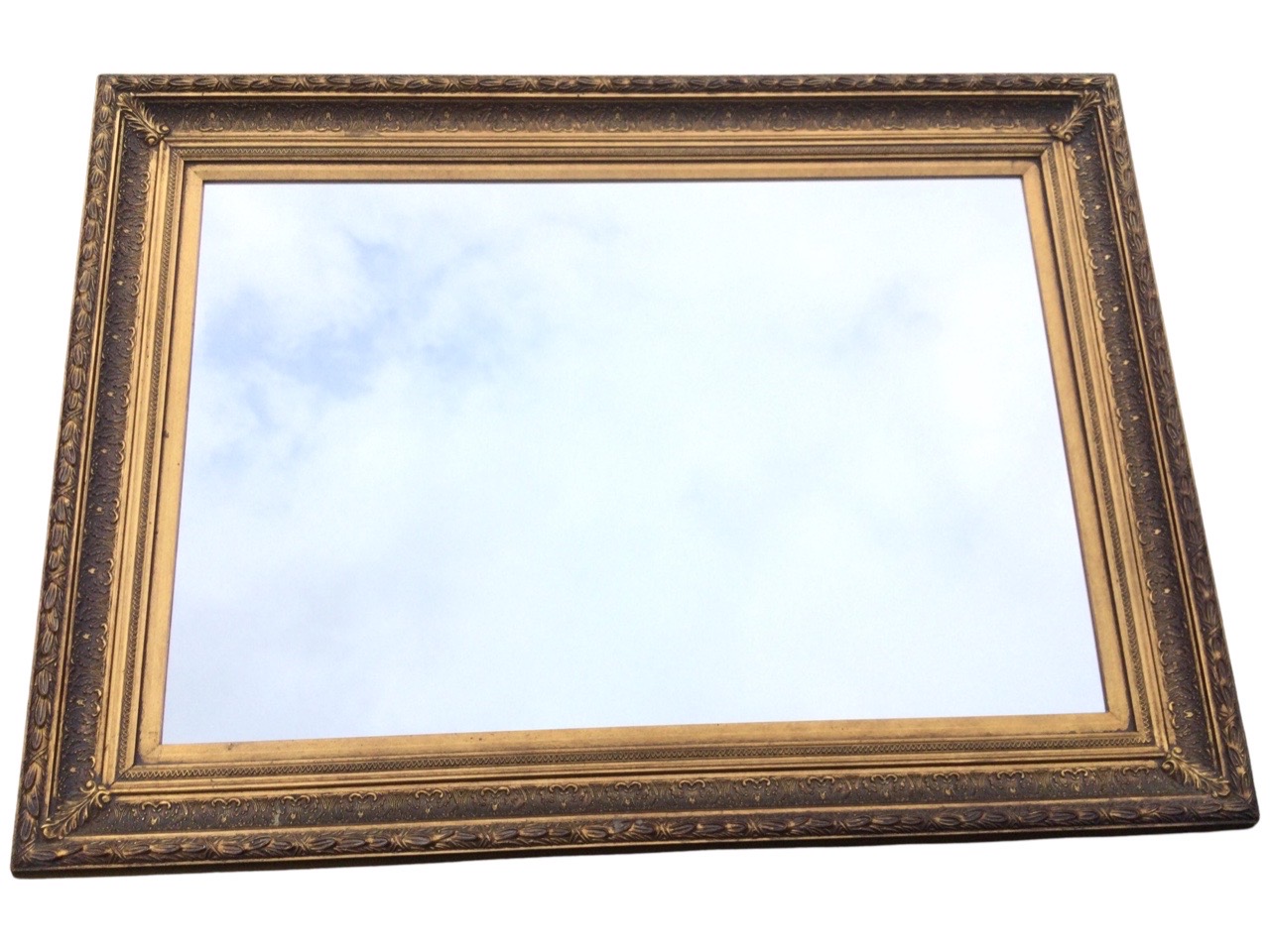 A rectangular gilt framed mirror, the frame with leaf and scroll embossed decoration. (44.75in x