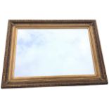 A rectangular gilt framed mirror, the frame with leaf and scroll embossed decoration. (44.75in x