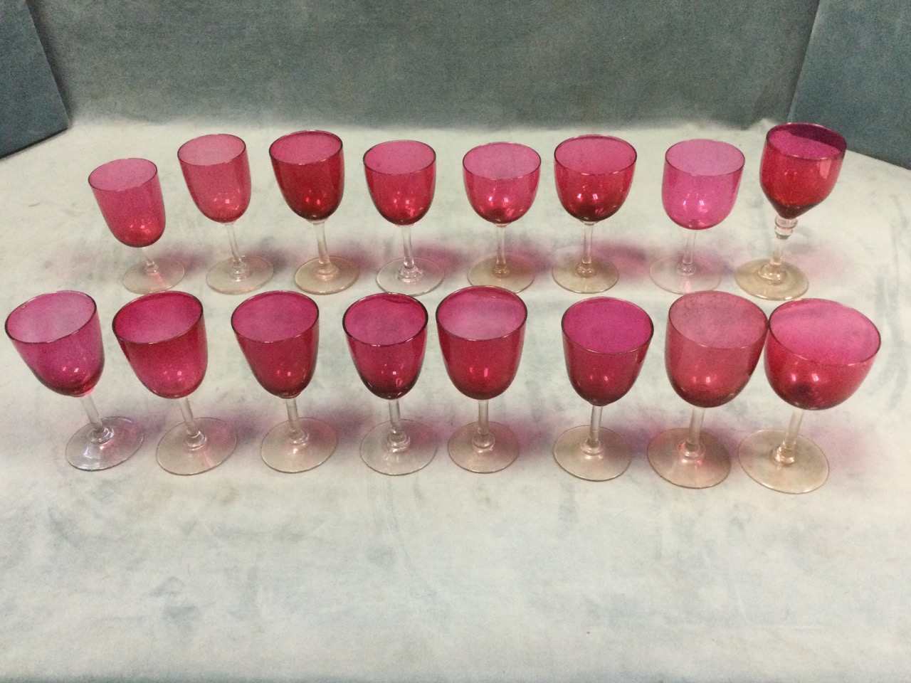 A set of sixteen cranberry wine glasses on clear stems with circular bases - varying shapes & sizes.
