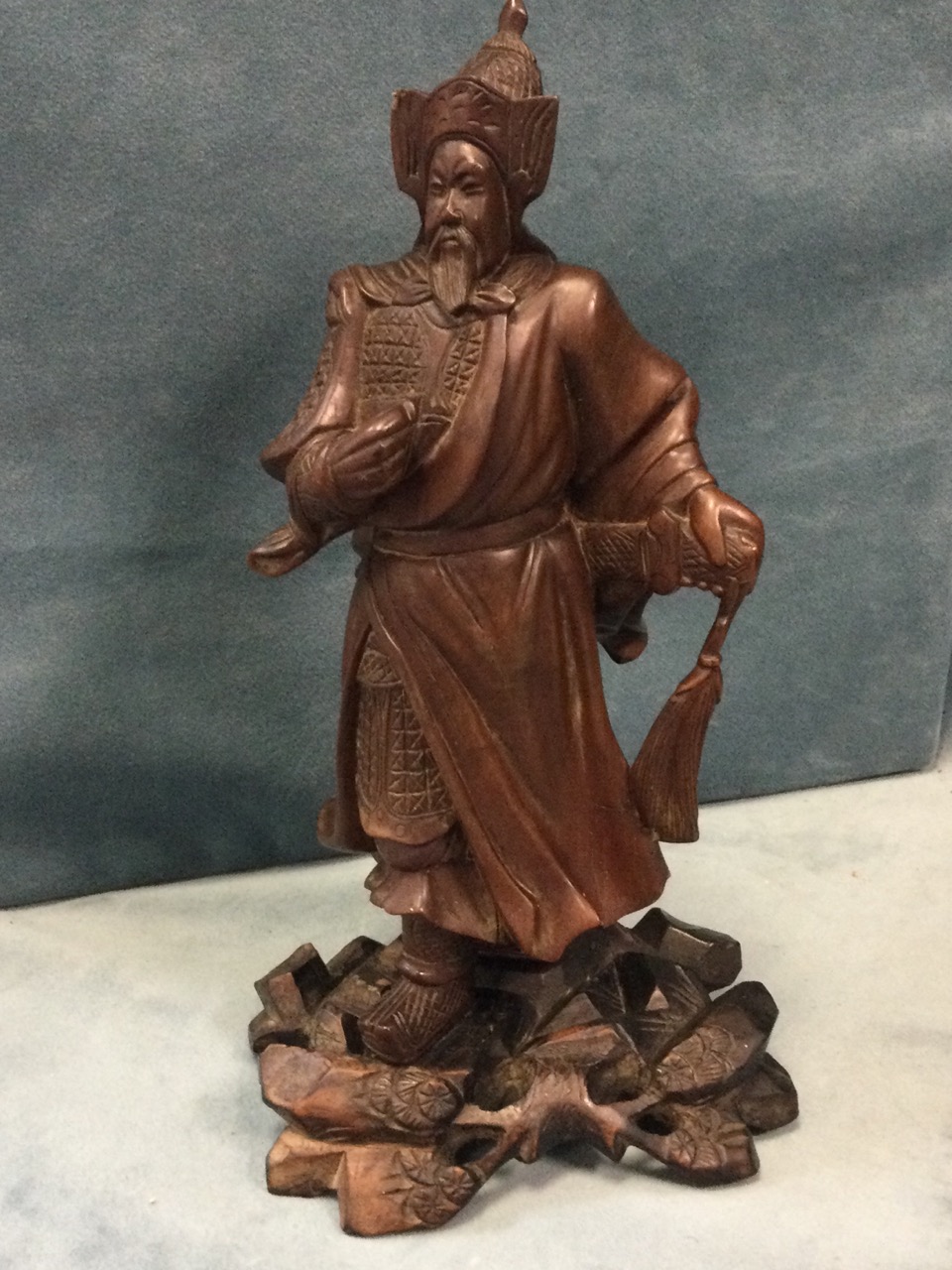 A Japanese carved figure of a warrior, the cloaked bearded man with stylised helmet having hand to