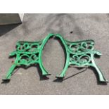 A pair of painted cast iron bench ends with scrolled decoration to channelled frames, raised on