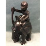 A large carved African elephant with inlaid eyes & feet, having seated boy atop holding batton. (