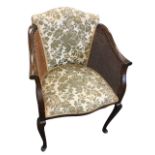A mahogany bergére armchair, the upholstered back framed by caned panels with downswept arms, the