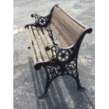 A cast iron garden bench with slatted back & seat, the scrolled arms above roundels with lion masks,