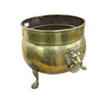 A cauldron shaped brass log bin with rolled rim and lionmask ring handles, raised on three paw feet.