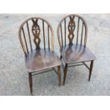 A pair of Ercol elm chairs with hooped backs framing pierced splats carved with oval fleur-de-lys,