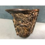 A carved nineteenth century horn libation cup decorated with two figures, rockwork, trees and