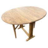 An oval elm Ercol drop-leaf dining table having leaves supported on square tapering gates, the table