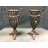 A pair of decorative fluted glass urn shaped vases with iron leaf mounted frames having scrolled