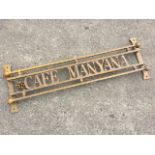 A gilded wrought iron sign - Cafe Manyana, the lettering framed by chamfered bars with ball