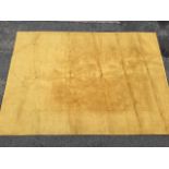 An Indian mustard coloured wool rug having plain central panel within a wide ribbed border. (111in x