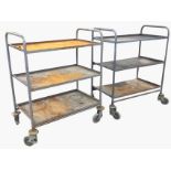 A pair of rectangular metal trolleys, each with three tray shelves on tubular frames with arched