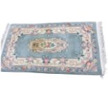 A Chinese thick pile wool rug woven with an oval floral medallion on pale blue ground, framed by