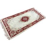 An Indian thick pile wool rug woven with ruby frieze and oval central medallion interlaced with