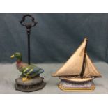 A painted cast iron duck doorstop with protruding handle; and a cast iron yacht flatback on wave