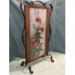 An art nouveau wrought iron framed firescreen on scrolled feet, the oak frame around an oil on