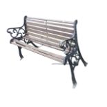 A cast iron garden bench with slatted back and seat framed by scrolled arms, raised on channelled