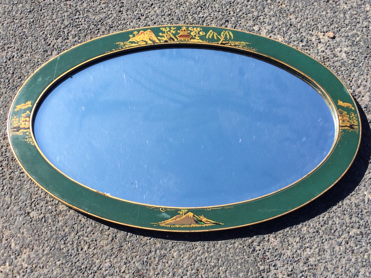 An oval lacquer framed mirror, the bevelled plate in green border framed by gilt bands, decorated