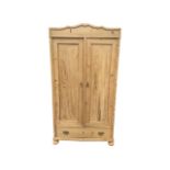 A Victorian style pine wardrobe, the arched scalloped pediment above two long panelled doors