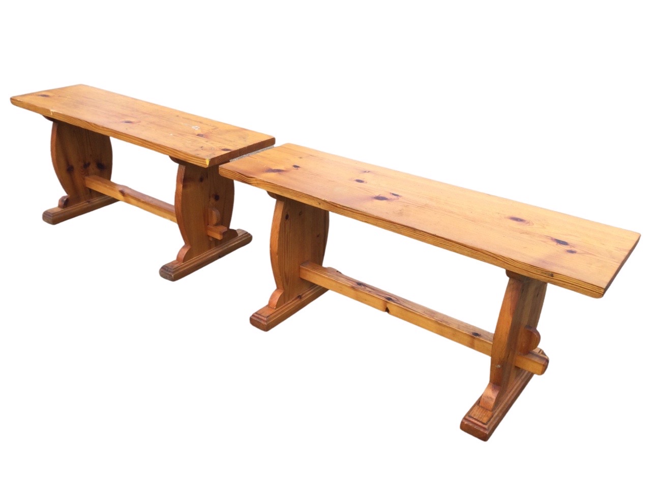 A pair of rectangular pine benches with plank seats on shaped trestle style supports joined by