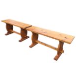 A pair of rectangular pine benches with plank seats on shaped trestle style supports joined by