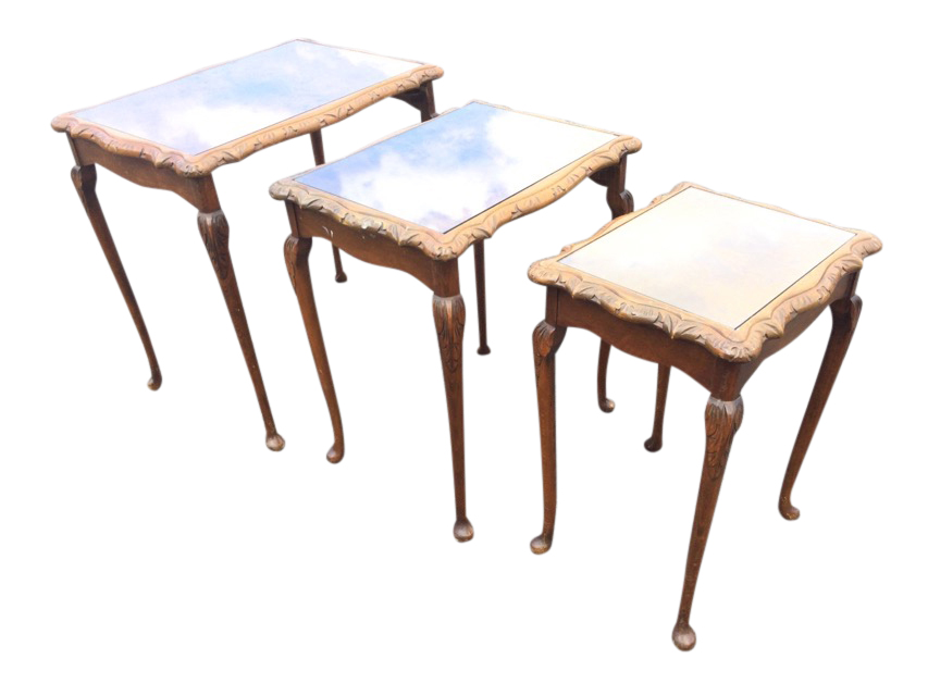 A nest of three walnut coffee tables with chisel carved scalloped tops framing glass panels,
