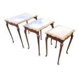 A nest of three walnut coffee tables with chisel carved scalloped tops framing glass panels,