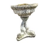 A composition stone garden urn with circular leaf moulded bowl on entwined dolphin support, above