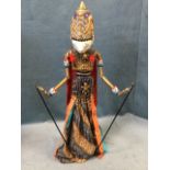 A boxed oriental rod puppet with carved headdress and articulated arms on sticks, the figure on