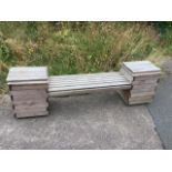 A rectangular pine garden bench with slatted rounded seat between two square tubs having rectangular