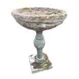 A composition stone birdbath with circular moulded bowl on slender baluster shaped column, above a