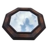 An octagonal oak framed mirror with bevelled plate, the angled frame with pressed flowerhead