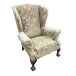 A Georgian style wing armchair with padded back and shaped arms above a sprung seat, raised on