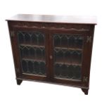 An oak cabinet with carved crescent frieze above leaded glass doors enclosing adjustable shelves,