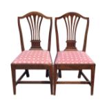A pair of antique mahogany dining chairs with arched shield backs above pierced splats, having