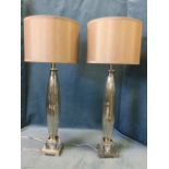 A pair of contemporary ribbed silvered glass tablelamps with fabric shades, on glass mirrored
