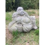 A smiling carved granite buddha type figure, the pot-bellied man seated against cushion holding a