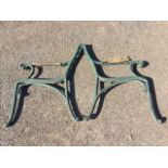 A pair of cast iron garden bench ends, the scrolled arms inset with wood elbow rests, raised on