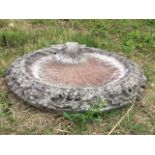 A circular composition stone garden birdbath, the bowl cast as a shell with scrolled segment, framed