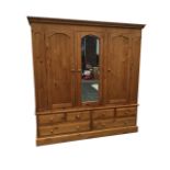 A large pine wardrobe with moulded cornice above three arched doors - the central one with