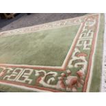 An Indian thick pile wool rug with green field framed by scrolled greek key style border in