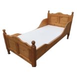 A pine single bed with arched panelled headboard & tailboard, having square cornerposts with ball