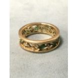 A gold eternity ring, the pierced band set with alternating elliptical emeralds and diamonds.